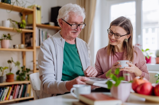 An elderly mand and his live-in carer reading a book togerther.