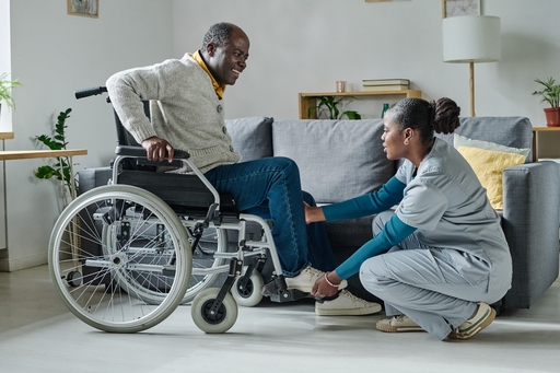 A live-in nurse helping aa man in a wheelchair with some exercise.